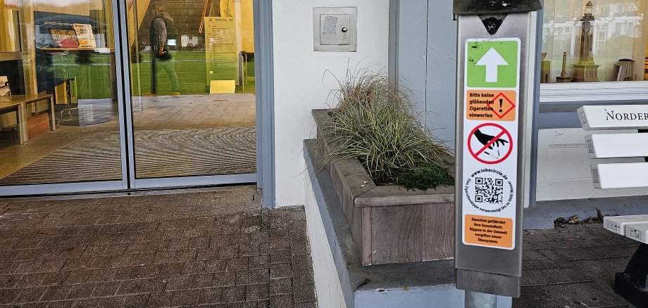 Das Bild zeigt einen Zigarettenkippensammler, der vor dem Rathaus steht
